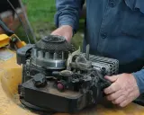 Ręce majsterkowicza przy silniku kosiarki Briggs & Stratton.