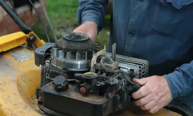 Ręce majsterkowicza przy silniku kosiarki Briggs & Stratton.