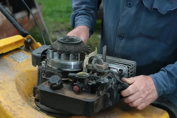 Ręce majsterkowicza przy silniku kosiarki Briggs & Stratton.